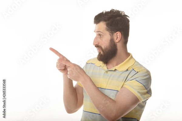 Fototapeta Young man in shirt pointing to the side with a finger to present a product or an idea while looking forward smiling on isolated white background 