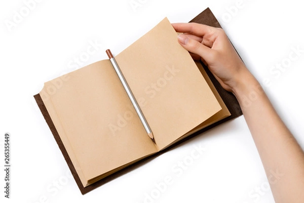 Fototapeta female hand turns over a page of an open craft notepad on which lies a gray pencil on a white background
