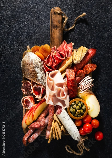 Fototapeta Assortment of salami and snacks. Sausage Fouet, sausages, salami, paperoni. On a black wooden background. Top view. Free space for your text