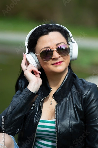 Fototapeta Brunette sits on a street bench and listens to music on headphones