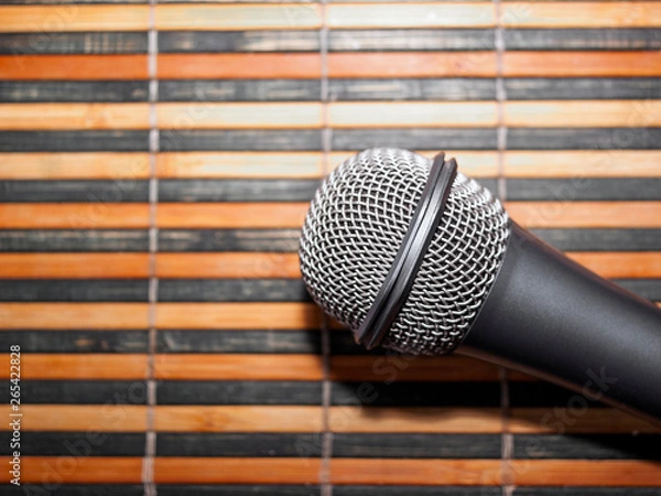 Fototapeta Top-Down View of A Microphone Head and Silver Grille on A Striped Yellow and Black Bamboo Mat Background. Karaoke Bar, Party Concept. Copy Space.