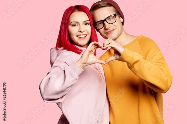Fototapeta  Happy couple young guy and girl dressed in stylish hoodie showing heart . 
