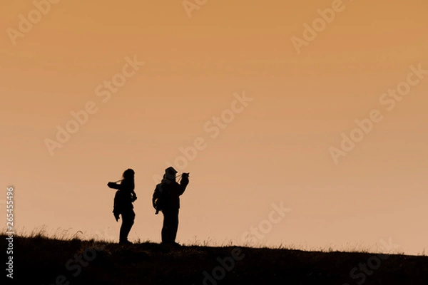 Fototapeta Silhouettes of hikers with backpacks enjoying sunset view from top of a mountain
