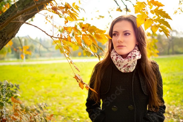 Fototapeta Beautiful romantic girl with perfect skin in autumn park, enjoying the perfect weather in a sunny day. Gorgeous young woman outdoors. Close-up shot in natural light, retouched, vibrant colors