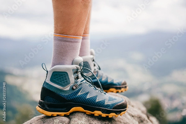 Obraz Zdjęcie nastroju męskich nóg w sportowych butach turystycznych z silną ochronną podeszwą. Męskie nogi w obuwie trekkingowe do podróży górskich stojących na kamiennym na zewnątrz na naturze na abstrakcyjnym tle.