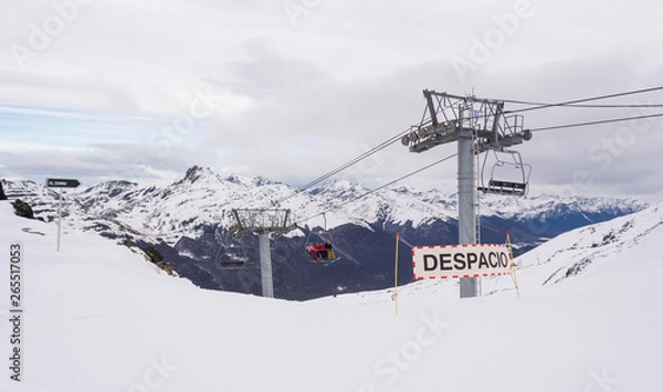 Obraz View of a ski slope with some warning signs and a chairlift on Castor ski center, on a cloudy winter day, with a mountain range on the background. Ushuaia, Tierra del Fuego, Argentina