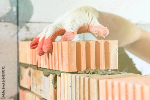 Obraz master with a tool, stacks a red brick. there is illumination and toning. shallow depth of cut.