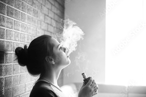 Obraz Vape teenager with  problem skin. Portrait of young cute girl smoking an electronic cigarette in the bar. Bad habit that is harmful to health. Vaping activity. Black nad white.