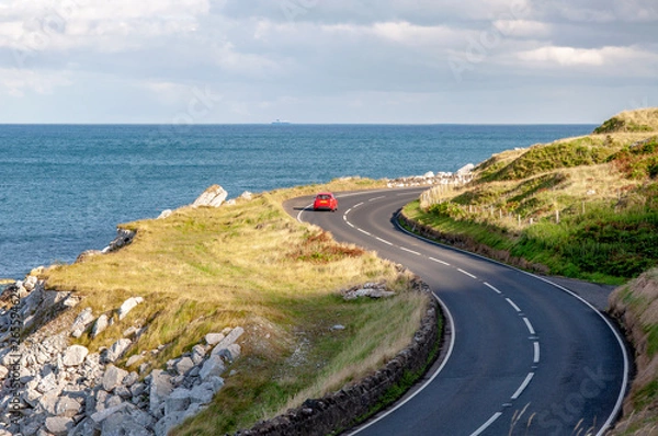 Fototapeta Wschodnie wybrzeże Irlandii Północnej i Antrim Coastal Road, a.k.a. Causeway Coastal Route z czerwonym samochodem. Światło słońca