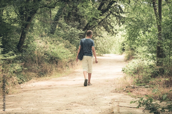 Obraz teenager with a bag on his shoulder goes to the forest.