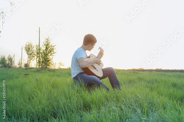 Obraz teen playing guitar outdoors in the summer on the background of birch trees.