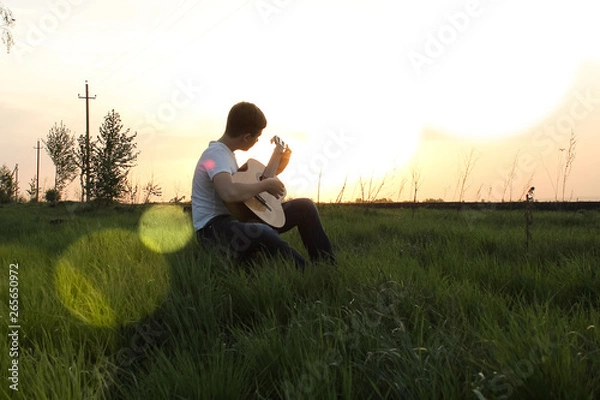 Obraz teen playing guitar outdoors in the summer on the background of birch trees.