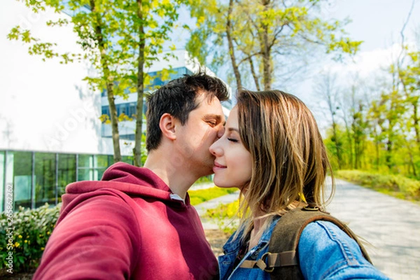 Fototapeta A young couple of Europeans kisses on the street. University building in the background. Spring time