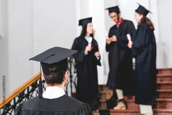 Fototapeta back view of student in graduation cap standing in university