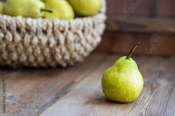 Fototapeta one fresh ripe organic yellow pear on rustic wooden brown table with defocused pears in basket on background. Selective focus. Horizontal copy space For design about agricilture, fruit, healthy food