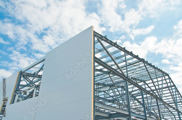 Fototapeta Metal frame of the building with a sandwich panel of insulation on the wall. Construction of a new industrial building.