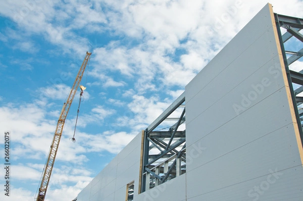 Fototapeta Metal frame of the building with a sandwich panel of insulation on the wall. Construction of a new industrial building.