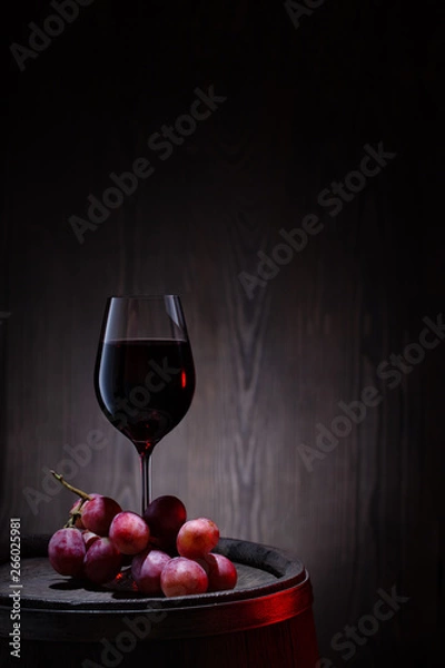 Obraz Glass of red wine and pink grapes on wooden barrel