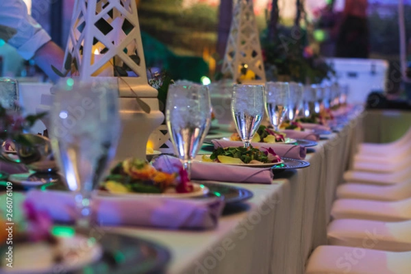 Fototapeta Elegant Plates and Crystal Wine Glasses set at Long Tables during an Event with Purple lighting