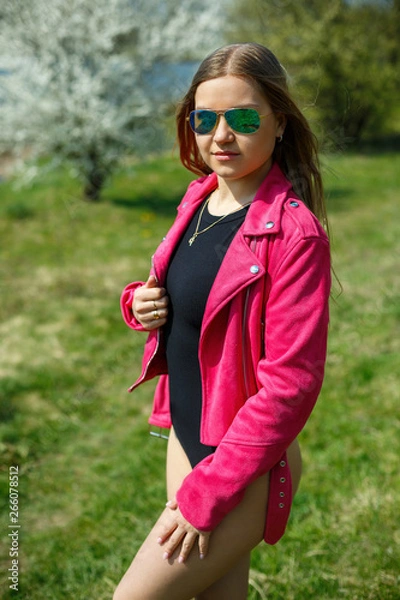 Fototapeta Girl in a black bodysuit and a pink jacket in nature with a flowering tree