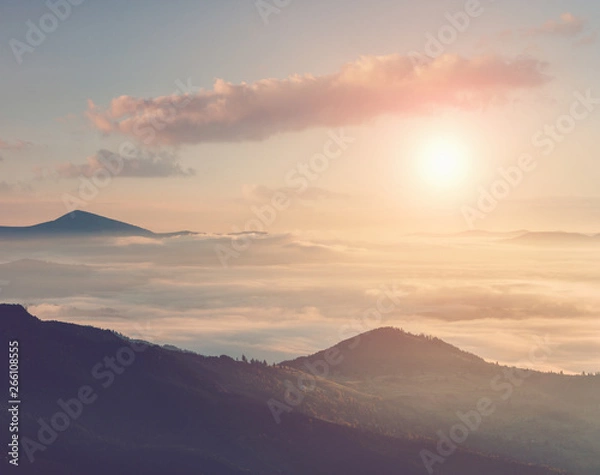 Fototapeta Beautiful landscape in the mountains at sunrise with haze and cloudy sky. View of magnificent natural scenery of mountains hills covered mist. Filtered image:cross processed retro effect.