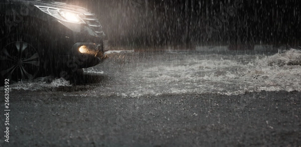 Fototapeta Car with headlights run through flood water after hard rain fall at night.