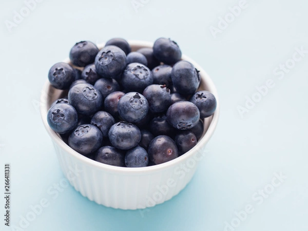 Fototapeta Fresh ripe blueberries in white bowl on a blue bright background