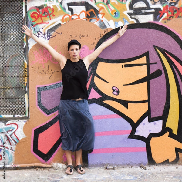 Obraz Jeune femme levant les bras devant un graffiti