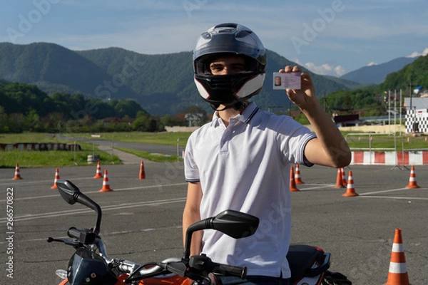 Obraz Młody człowiek w kasku na motocyklu pokazuje prawo jazdy
