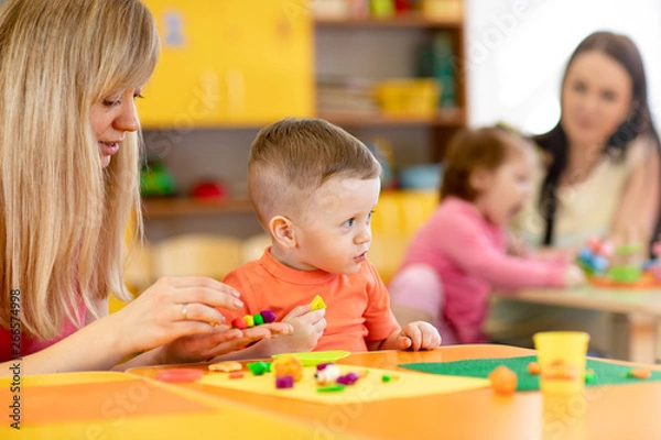 Fototapeta Kindergarten kid with teacher mould from plasticine on table in nursery