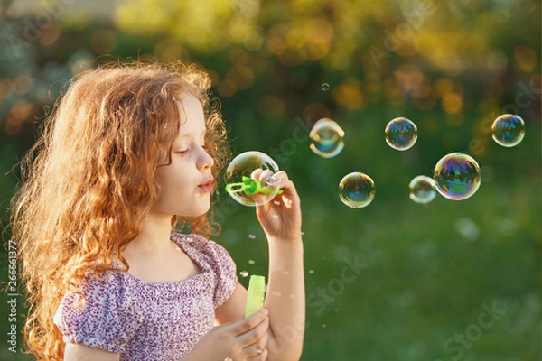 Obraz Little girl blowing soap bubbles in spring outdoors.