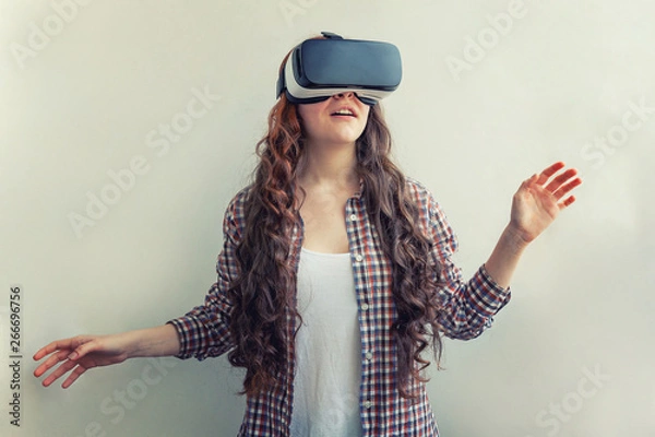 Fototapeta Smile young woman wearing using virtual reality VR glasses helmet headset on white background. Smartphone using with virtual reality goggles. Technology, simulation, hi-tech, videogame concept