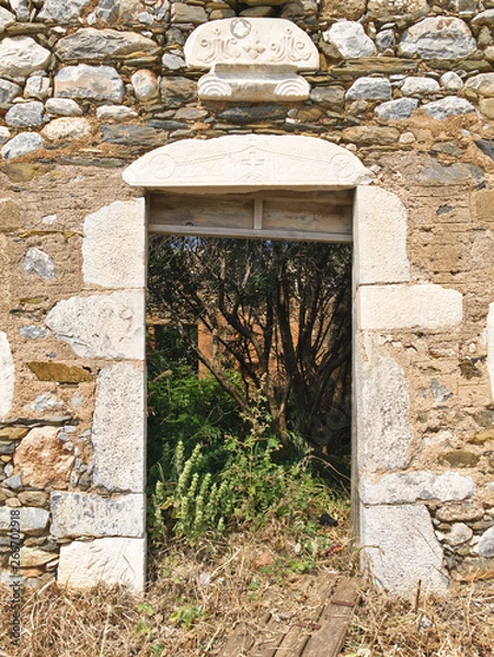 Fototapeta Building detail of fallen door on stone wall in Mani Greece with sybols above door opening.
