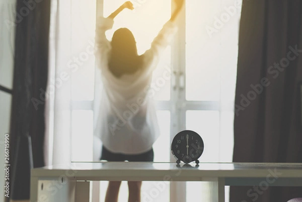 Obraz Blured of refreshing female in white shirt stretch lazy in bedroom after waking up at 6 o'clock in the morning,Alarm clock,Back view