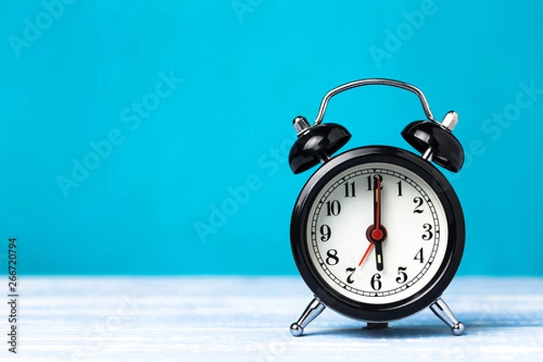 Obraz Retro black alarm clock on blue background with copy space. Alarm at 7 clock hand at 6