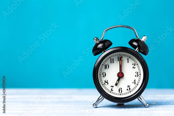 Obraz Retro black alarm clock on blue background with copy space. Alarm at 7 clock hand at 7