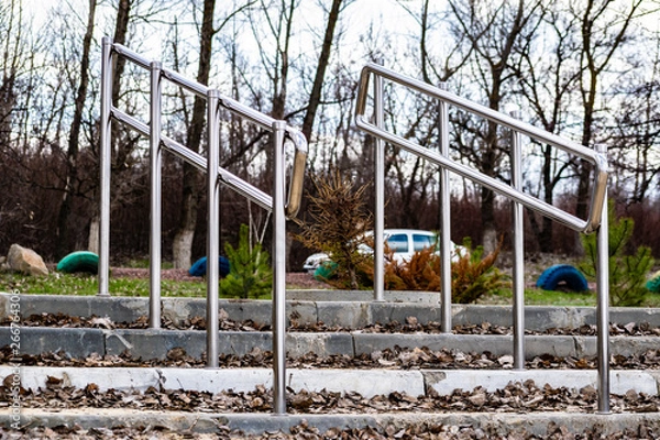 Fototapeta Modern embankment in the Rostov region, small railings and steps of gray concrete. Metal shiny stainless steel handles. The construction on nature, among trees in the usual clear day