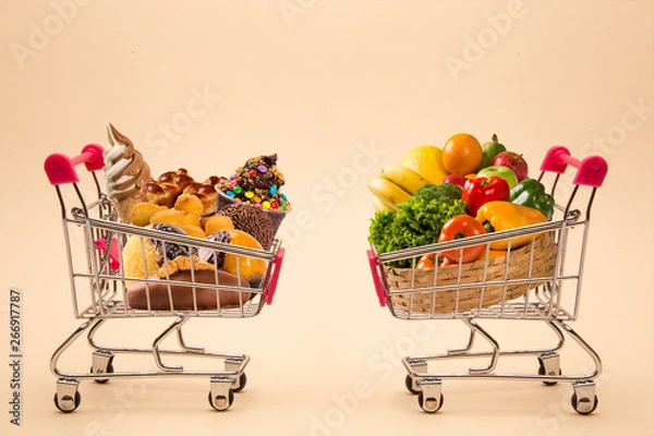 Obraz Concept of food and diet. Wafers, chocolate, ice cream and fruits and vegetables in shopping cart. Fast food addiction. Struggling with overweight and obesity. comparison between light food and fatten
