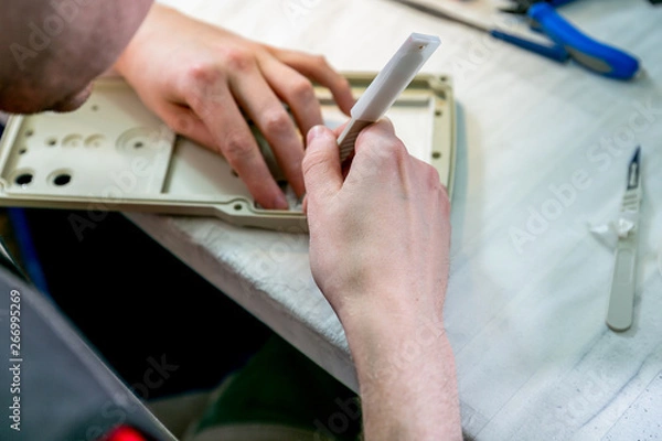 Obraz A worker sanding a plastic blank. Manufacturing of plastic products. Medium business concept. Hands close-up