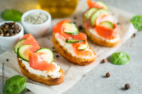 Fototapeta Salmon, cucumber and cream cheese bruschetta. Italian tapas, antipasti with vegetables, herbs and oil on grilled ciabatta and baguette bread. Sandwich.
