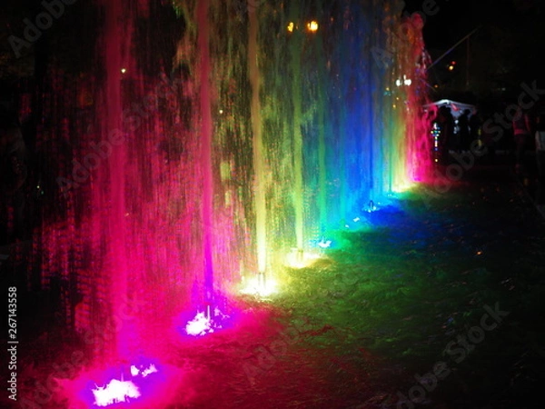 Fototapeta Blurred background of light fountain with round light bokeh at night.Beautiful multicolored dancing fountains at night.fountain with colorful illuminations at night.