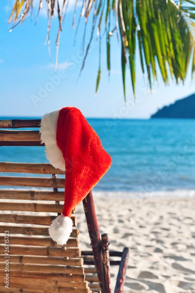 Fototapeta Red Santa's hat hanging on beach chair under palm tree
