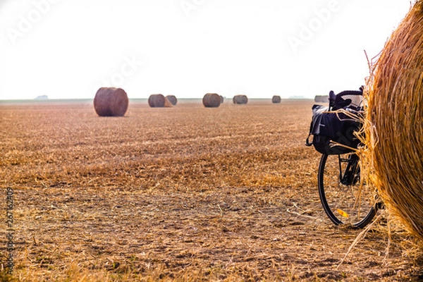 Fototapeta Touring bike hidden by a hay ball in a big orangee-colored field
