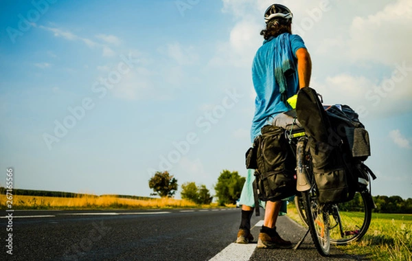 Fototapeta Cyclotourist facing backward and looking at a long road ahead of him