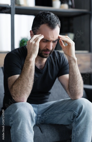 Fototapeta sad handsome man sitting on sofa with closed eyes and holding hands near head