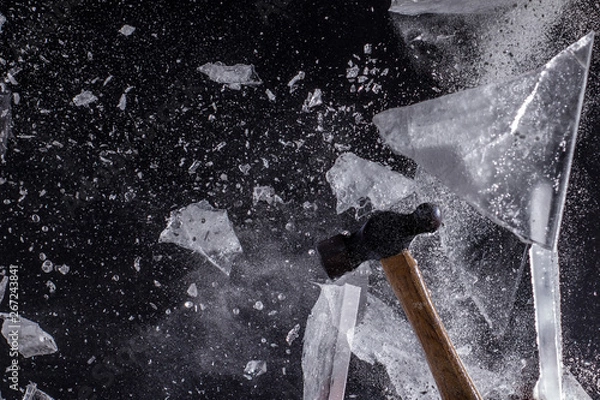 Fototapeta Moody, Shadowy High-Speed Photo of a Ball-Peen Hammer Smashing through a Sheet of Ice - Exploding in a Cloud of Dust and Shards with a Black Background