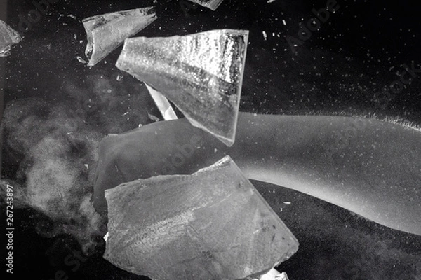 Obraz Moody, Shadowy High-Speed Photo of a Caucasian Man's Bare Fist Smashing through a Sheet of Ice - Exploding in a Cloud of Dust and Shards with a Black Background