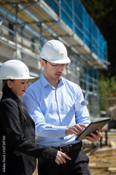 Fototapeta Two architects a man and a woman in construction in white helmets.