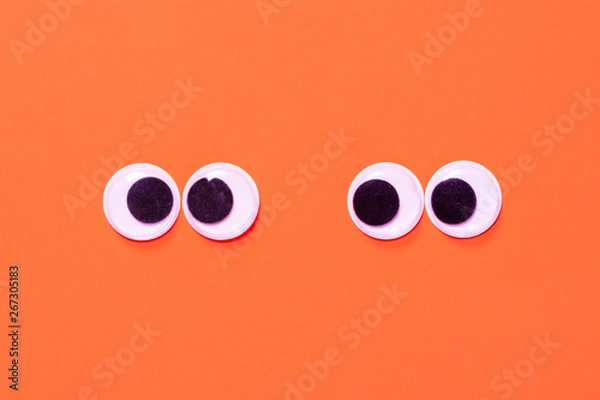 Fototapeta Googly eyes: One pair strabismus and squint mad googly eyes and one pair normal funny eyes next to each other on orange background.
