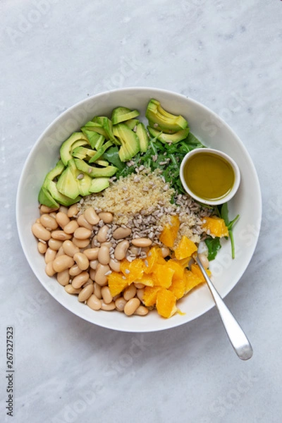 Fototapeta Vegetarian salad with avocado, white beans, arugula, spinach, sunflower seeds, orange and quinoa flavored with olive oil with lemon and Himalayan salt